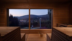 A sauna room with wooden benches and a large window offering a view of a town and mountains. - Ski & Spa Bellevue Harrachov (Harrachov)