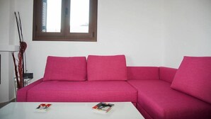 Un soggiorno moderno con un divano modulare rosa, un tavolino bianco con riviste e una finestra con persiane.