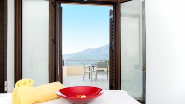 Una stanza con vista sulle montagne, un tavolo con una ciotola rossa e un asciugamano giallo, e un balcone con sedie.