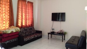 A living room with a sofa, ottoman, coffee table, TV, and curtains. - Nadrah Putrajaya Homestay (Putrajaya)