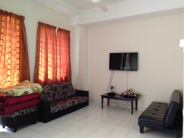A living room with a sofa, ottoman, coffee table, TV, and curtains. - Nadrah Putrajaya Homestay (Putrajaya)