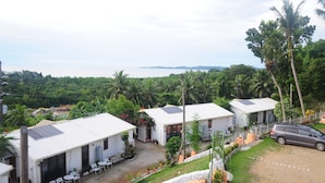 A residential area with multiple white houses, some with solar panels, surrounded by lush greenery and palm trees. - shell villa apartel resort (Koror)