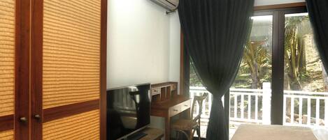 A hotel room with a bed, a TV, a desk, and a balcony with a view of the outdoors.
