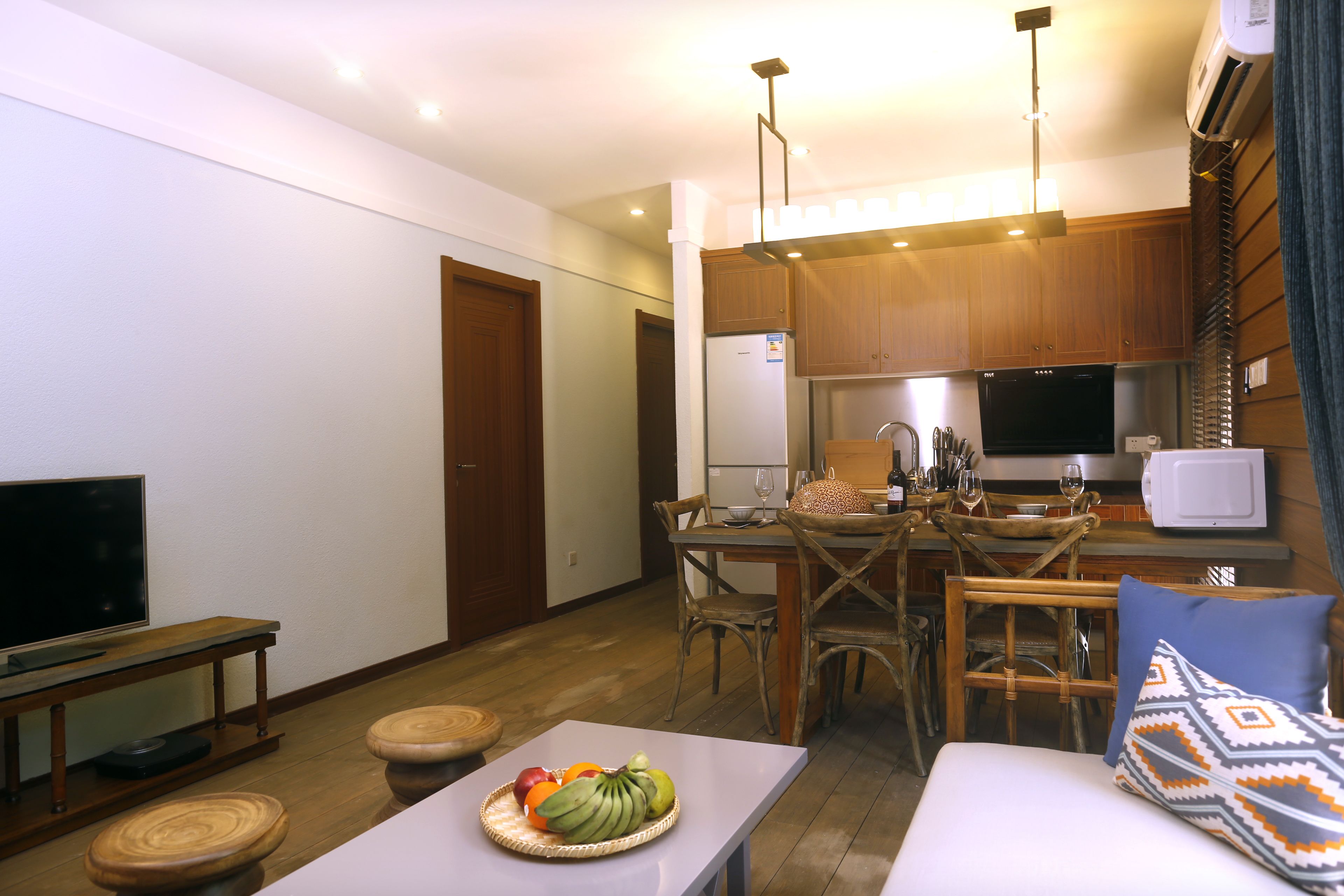A compact living space with a dining area, kitchenette, and a seating area with a TV and a fruit basket.