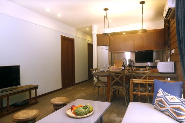 Un espace de vie compact comprenant un coin repas, une kitchenette et un coin salon avec un téléviseur et un panier de fruits.