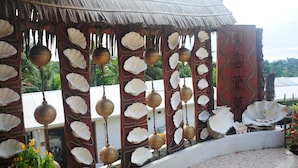 A traditional structure with a thatched roof, decorated with hanging brass bells and white shell ornaments. - shell villa apartel resort (Koror)