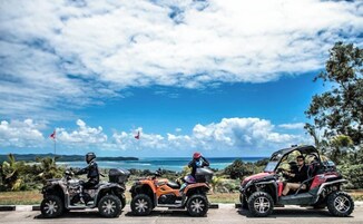 Tres vehículos todo terreno estacionados en una carretera con una vista panorámica del océano y palmeras.