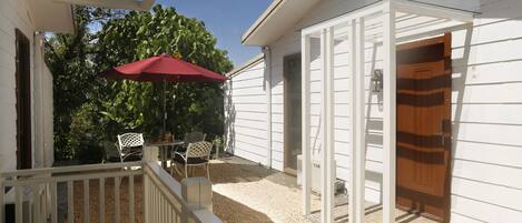 A covered patio with a red umbrella, a white railing, and a wooden door.