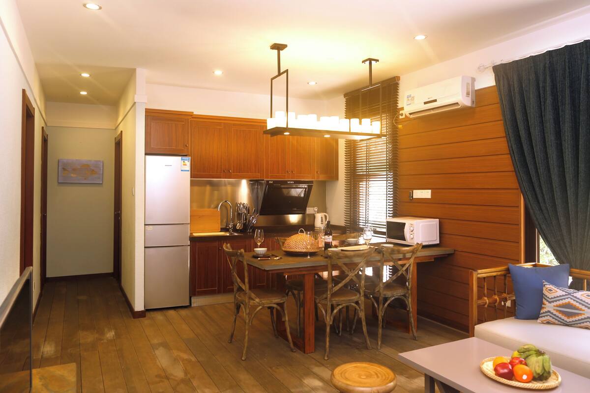 A compact kitchen with wooden cabinets, a refrigerator, a microwave, and a dining area with a table and chairs.