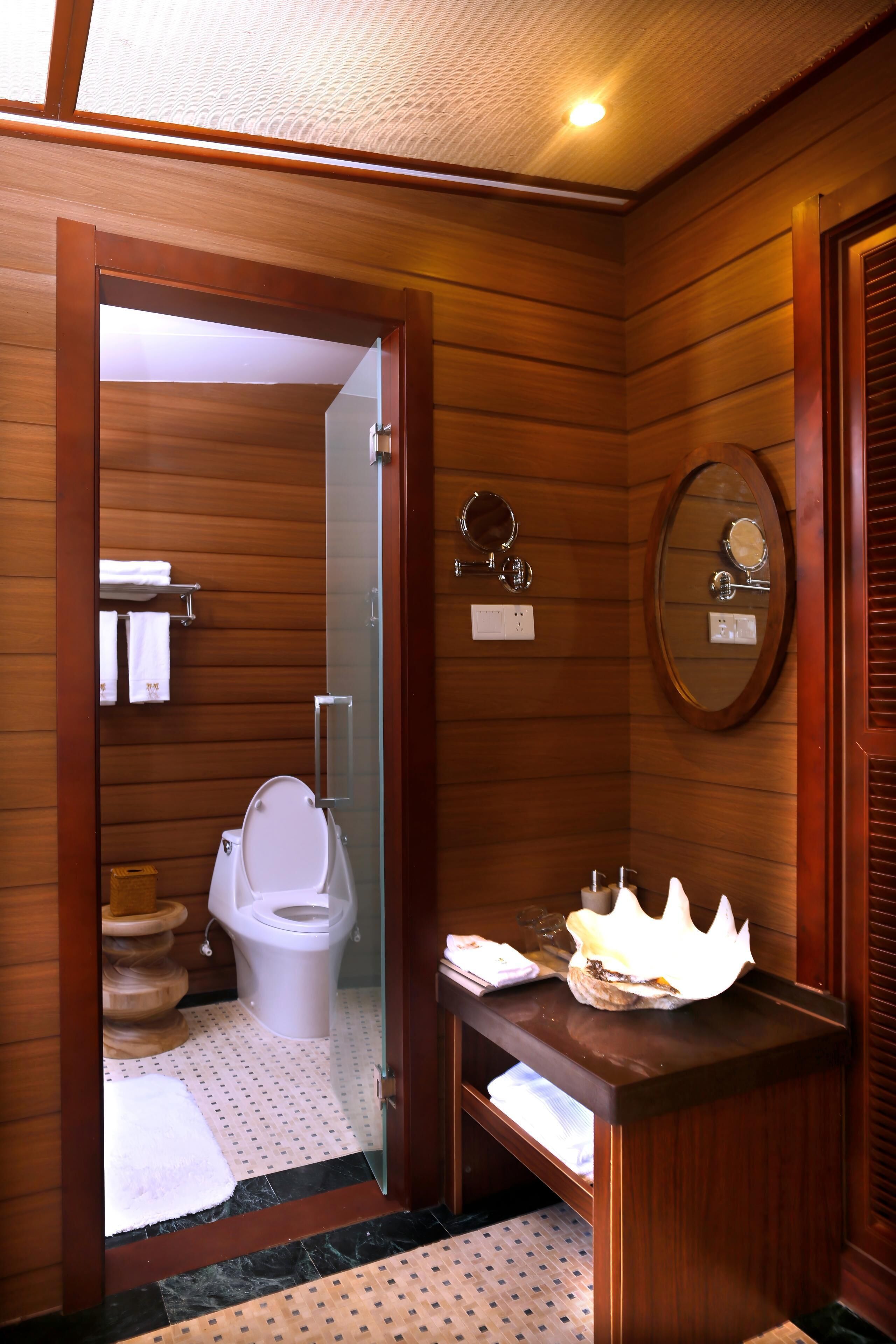 A wooden-paneled bathroom with a toilet, a sink with a mirror, and a shower area.