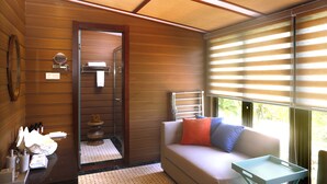 A cozy room with a wooden ceiling, a sofa with cushions, a small table, and a window with blinds. - shell villa apartel resort (Koror)