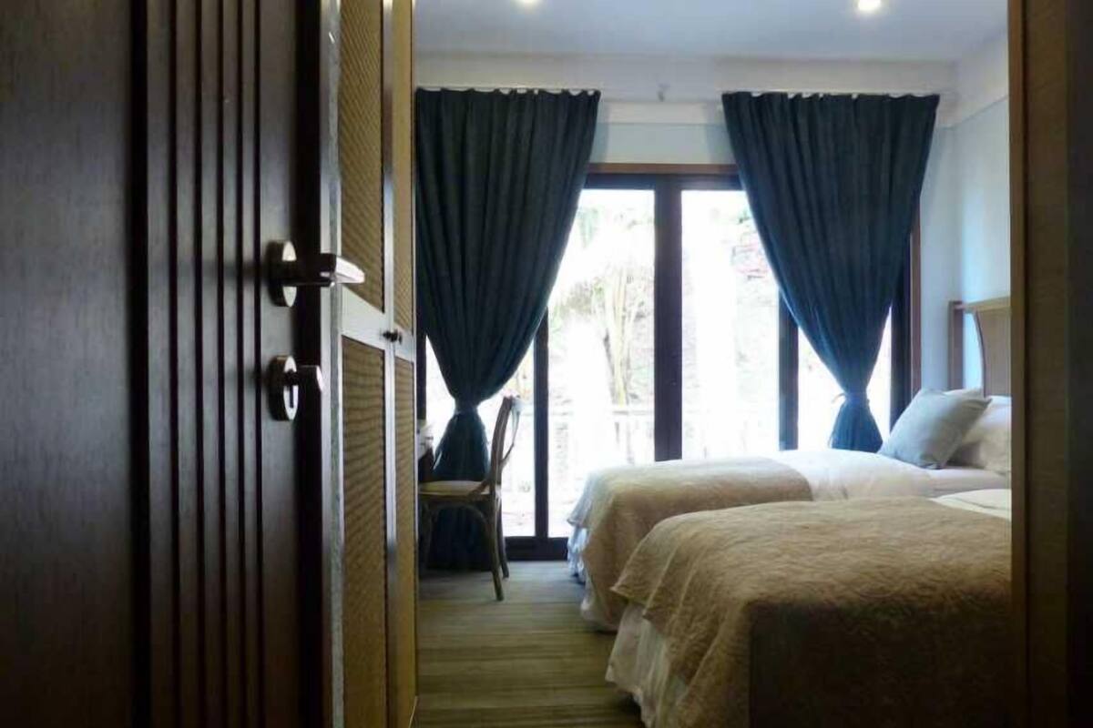 A hotel room with two beds, a wooden floor, and a view through a glass door.