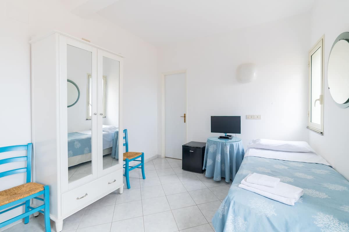 Un dormitorio con cama, armario, silla, escritorio con computadora y televisión.