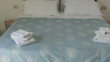 Una cama bien hecha con cubrecama azul y almohadas blancas, una obra de arte enmarcada en la pared y una mesita de noche con una lámpara.