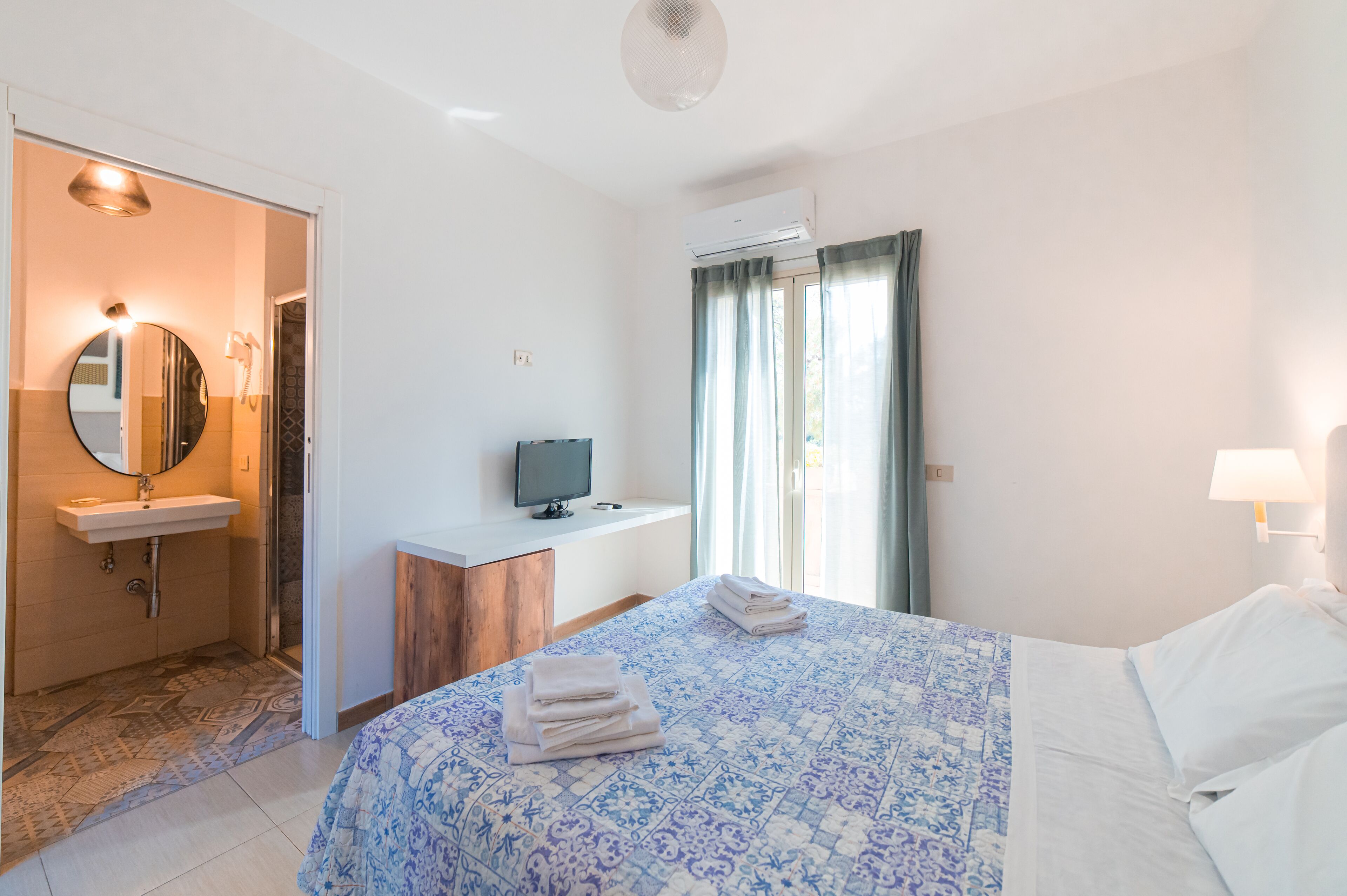 Una habitación de hotel con cama, escritorio, computadora, lavamanos y espejo.