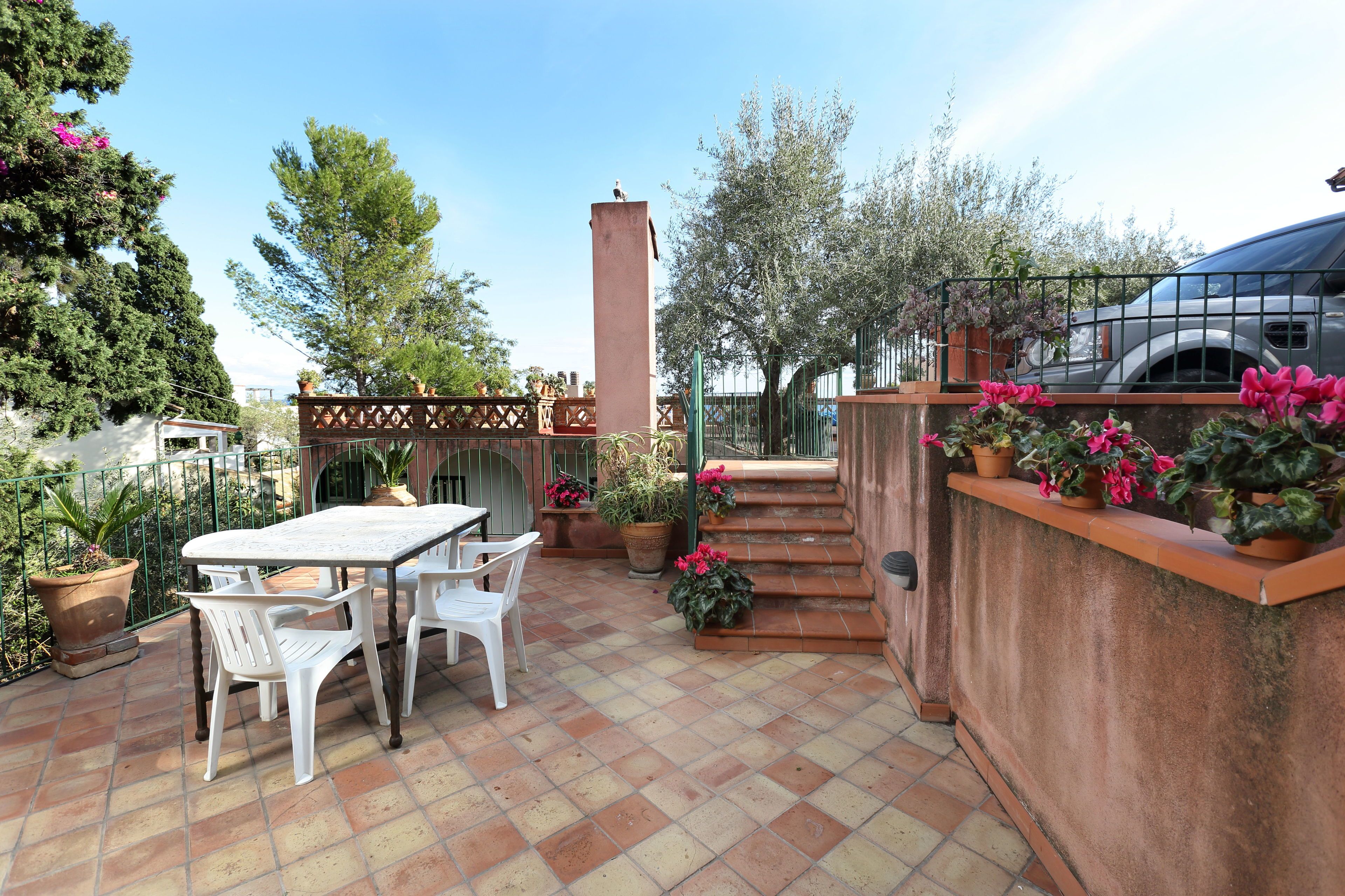 A patio area with a table and chairs, potted plants, and a staircase leading to a higher level.
