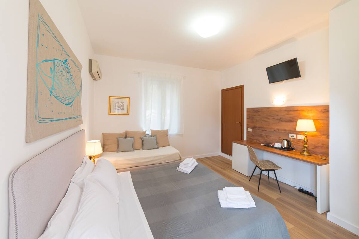 Habitación de hotel con cama, escritorio, silla, televisor y un cuadro en la pared.