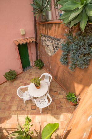 A small patio with a round table and chairs, surrounded by potted plants and a tiled floor. - Hotel Villino Gallodoro (Taormina)