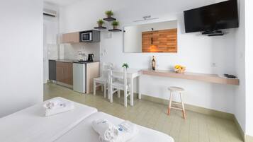 Una habitación de hotel moderna con kitchenette, televisor montado en la pared y un pequeño rincón de estar con una silla y un taburete.