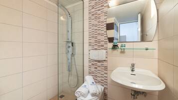 A modern bathroom with a glass shower enclosure, a white sink, and a mirror above it.