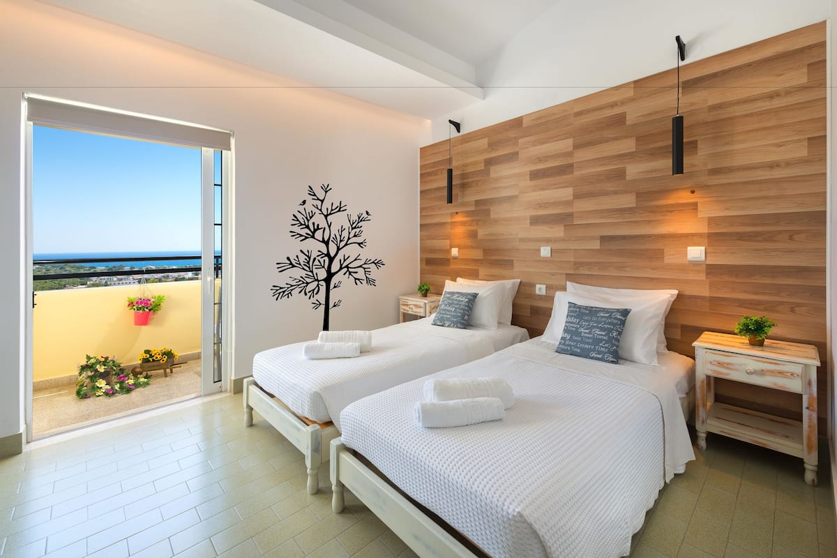 Un dormitorio moderno con dos camas, una pared de acento de madera, un balcón con flores y vistas a la ciudad.