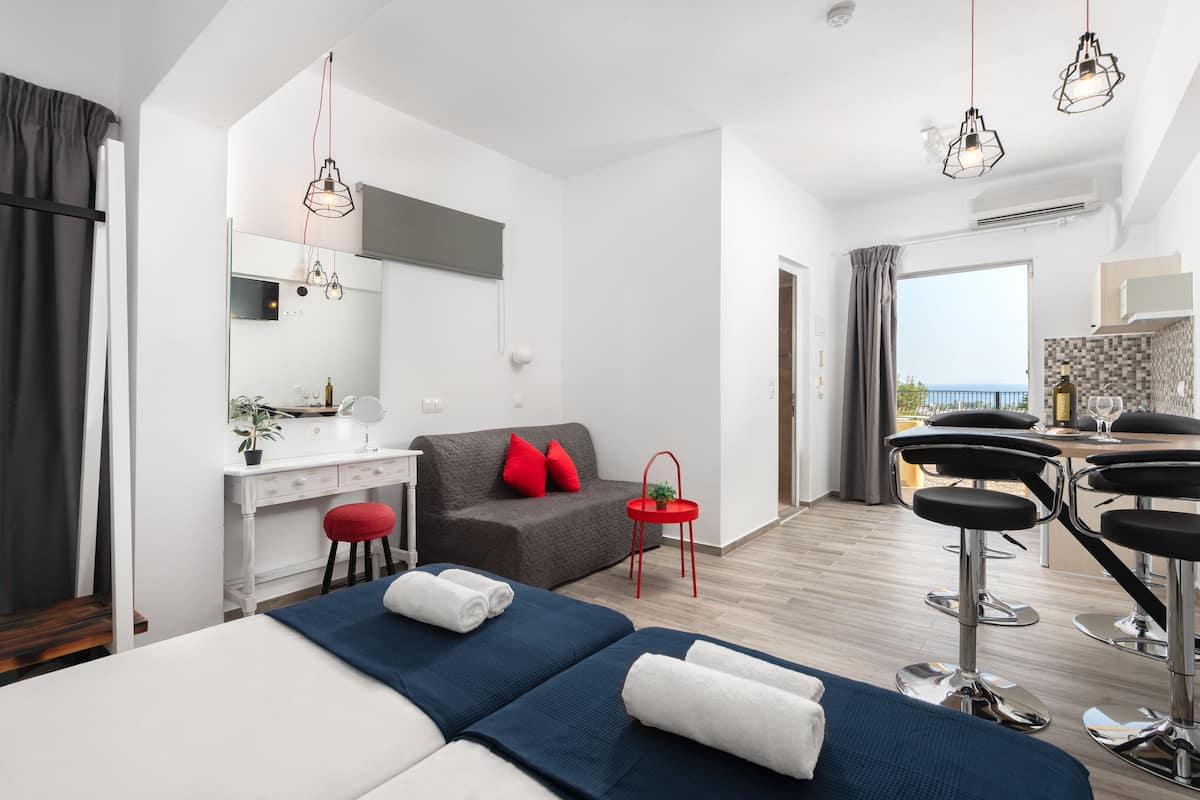 Una habitación de hotel moderna con cama, escritorio, sofá, una mesita con una planta y un balcón con vistas.