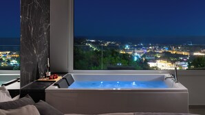 A modern bathroom with a large bathtub, a marble column, and a city view. - Pefkos View Suites & Maisonette (Rhodes)