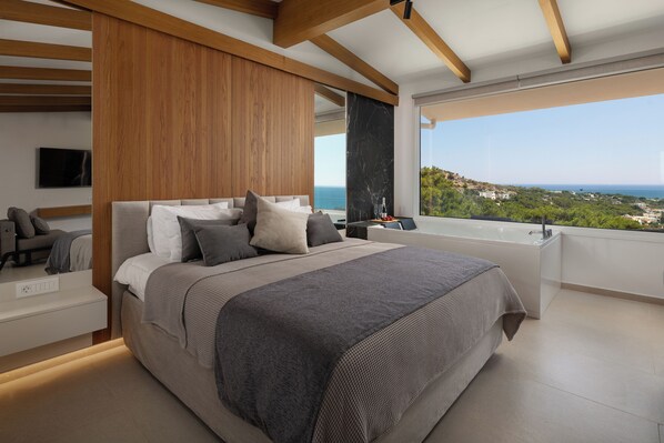 A modern bedroom with a large bed, a view of the sea, and a bathtub.