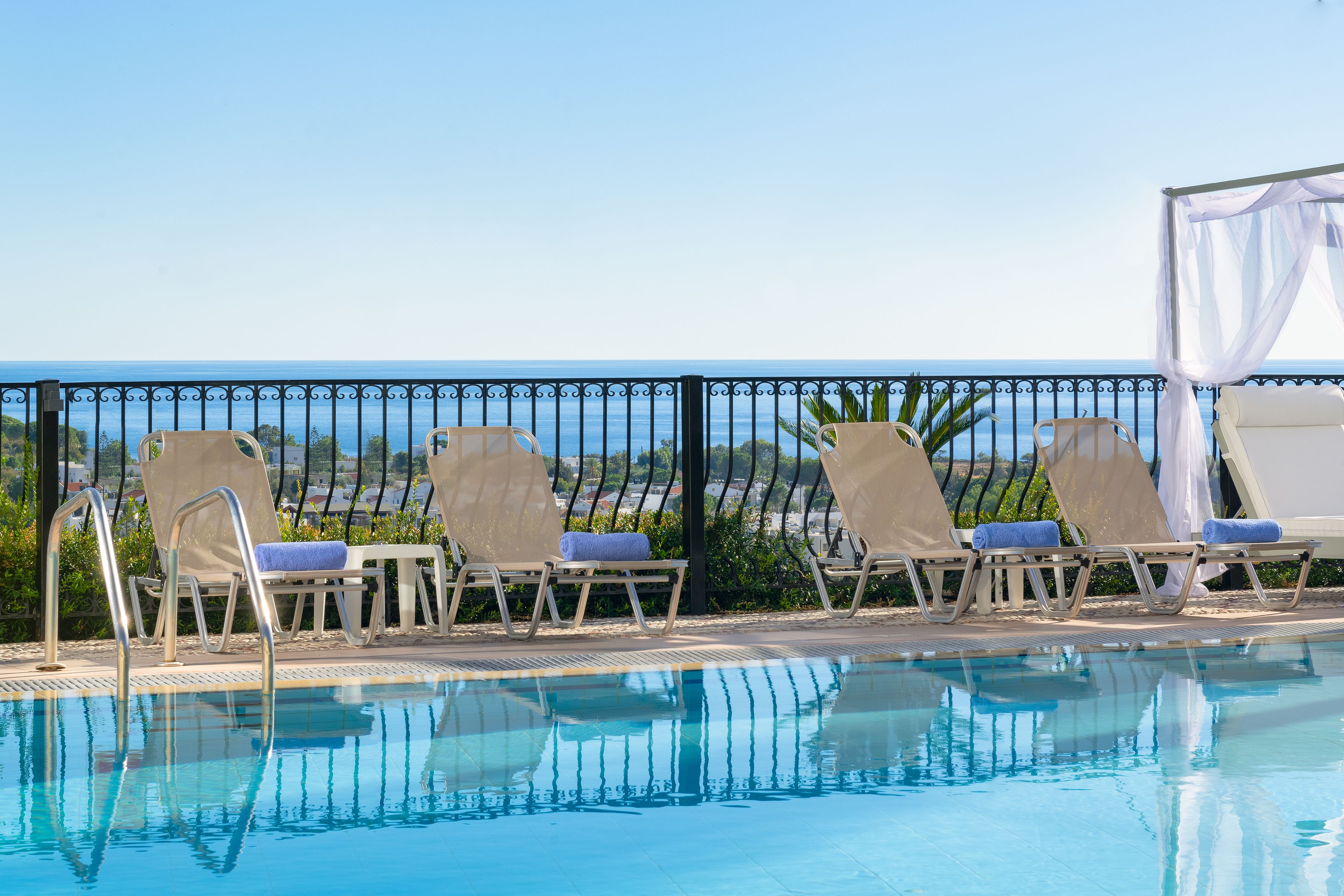 Zona de piscina con sillones reclinables y una pérgola, con vistas al mar.