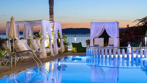 A pool area with lounge chairs, a canopy, and a view of the sea at dusk. - Pefkos View Suites & Maisonette (Rhodes)