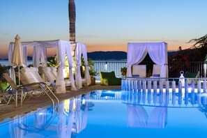 A pool area with lounge chairs, a canopy, and a view of the sea at dusk.