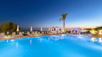 Relax by the serene pool surrounded by lounge chairs and umbrellas, with a palm tree and stunning views of the horizon.