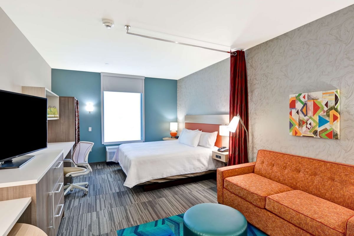 A hotel room with a bed, desk, TV, and a couch.