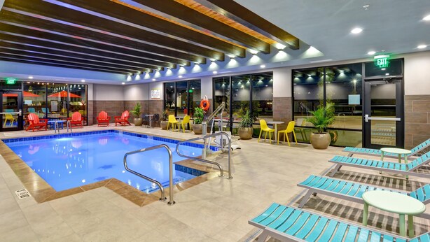Una piscina interior con sillones y mesas, una entrada con puerta de vidrio y un techo con vigas de madera.