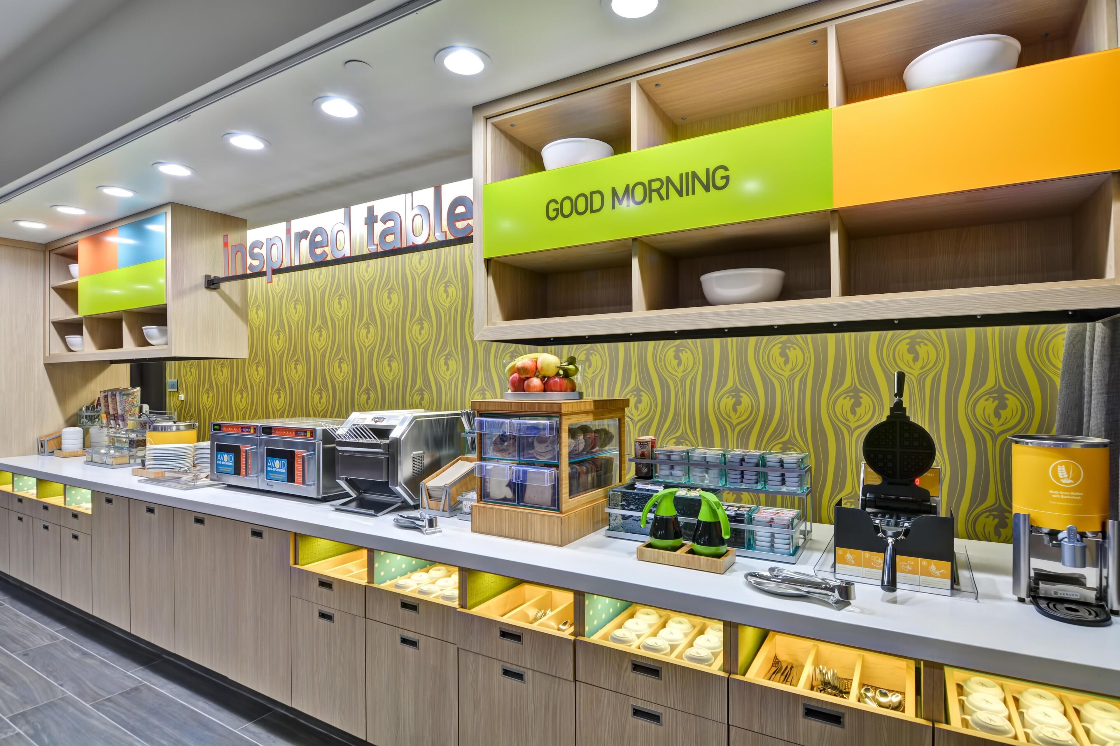 A breakfast buffet area with a 'Good Morning' sign, a self-service beverage station, and a variety of food items displayed in clear containers.