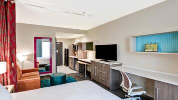 A hotel room with a bed, a desk, a TV, a mirror, and a kitchenette.