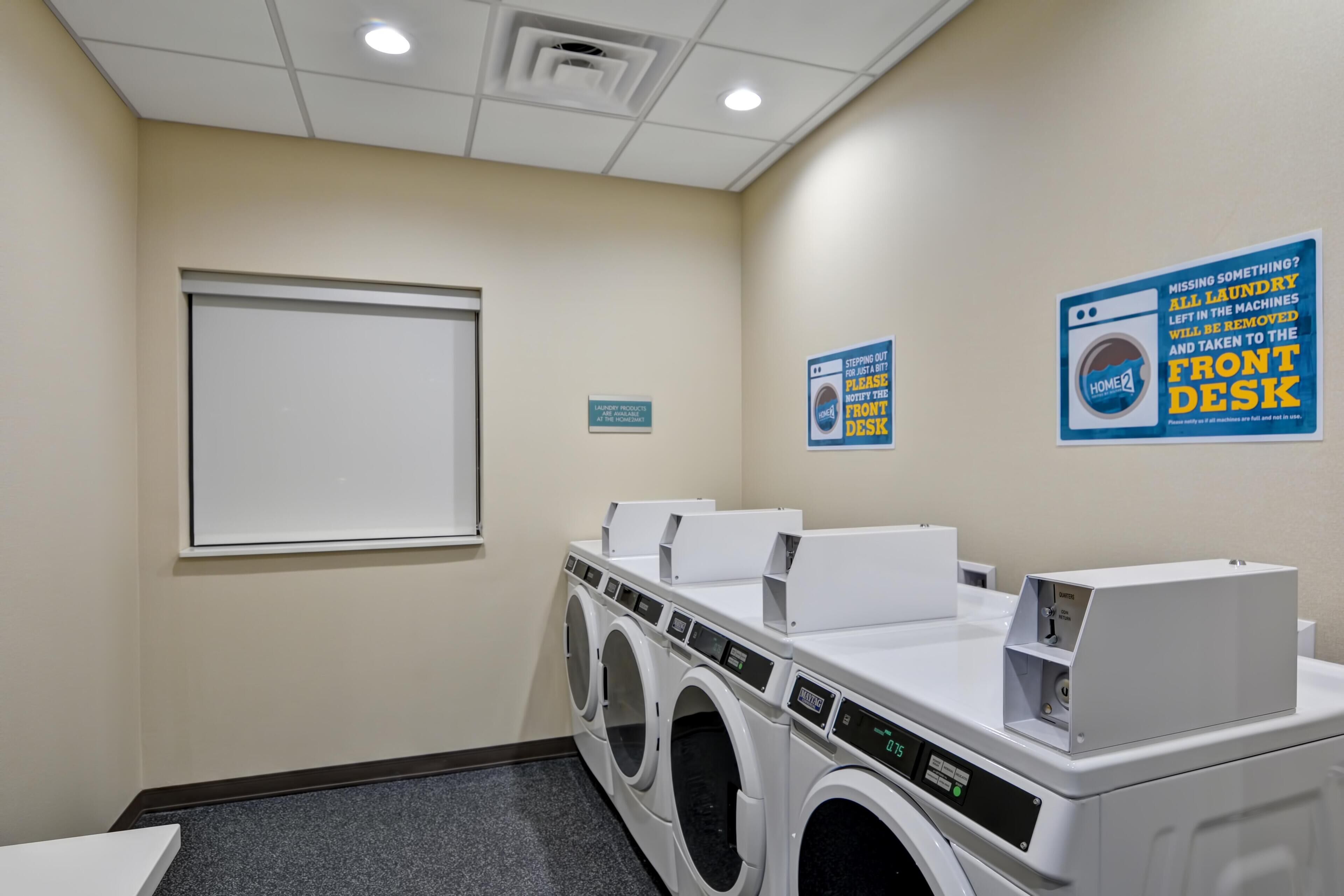 A laundry room with multiple washing machines, a front desk sign, and a window.