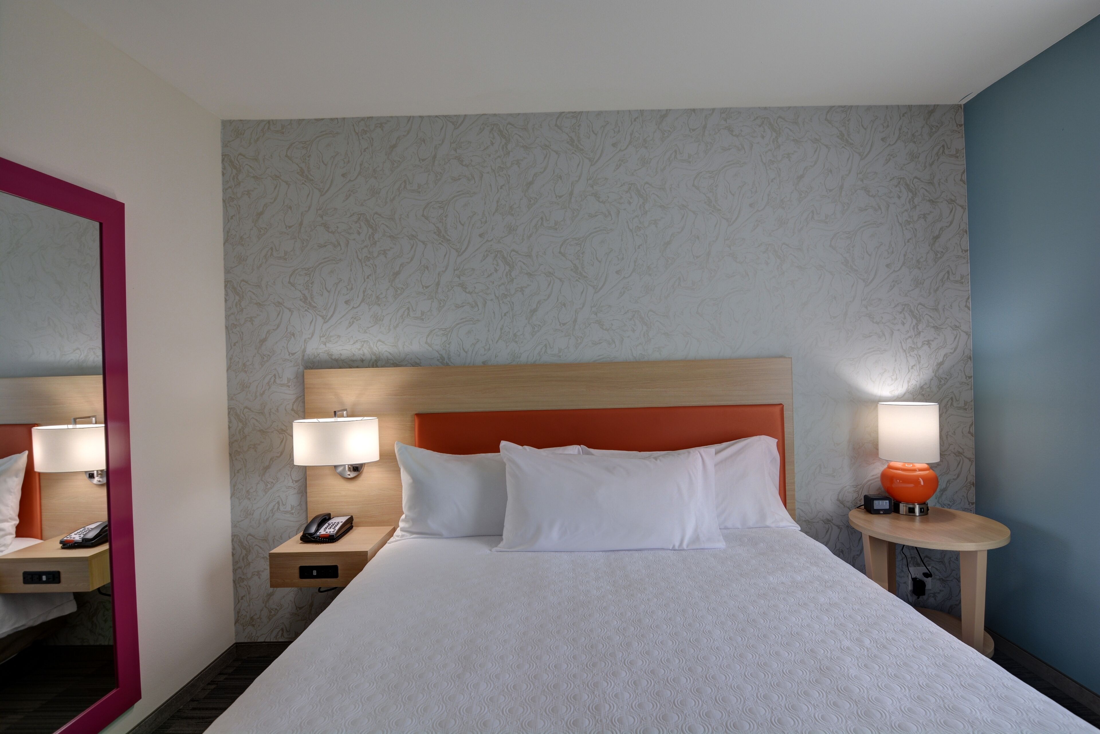 Une chambre d’hôtel avec un grand lit, deux tables de chevet avec des lampes, un téléphone et un miroir.