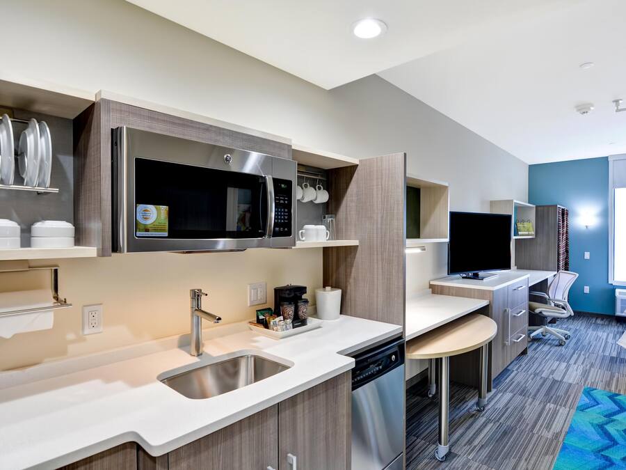 A modern kitchen with a microwave, sink, and dishwasher, a small dining area, and a view of the room.