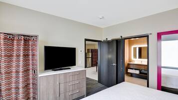 Un dormitorio con una cama, un televisor sobre un tocador, un armario y un baño visible a través de una puerta abierta.