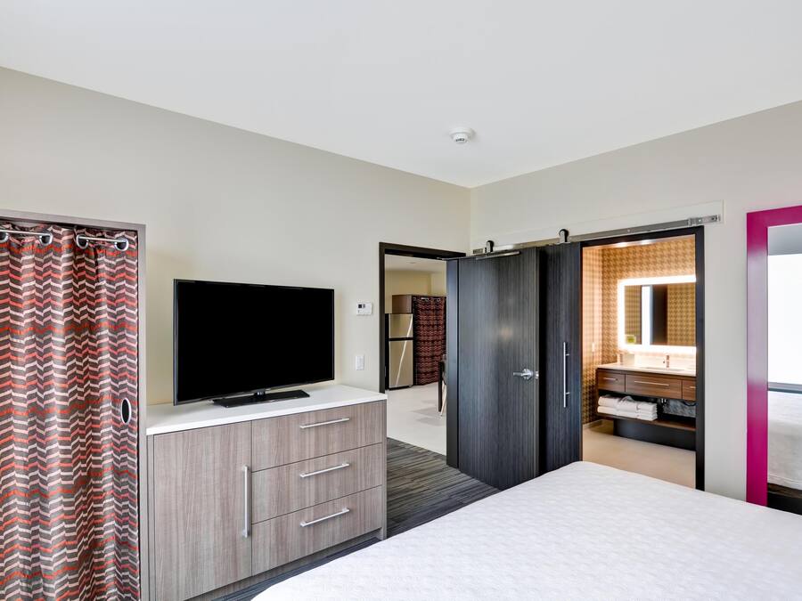 Un dormitorio con una cama, un televisor sobre un tocador, un armario y un baño visible a través de una puerta abierta.