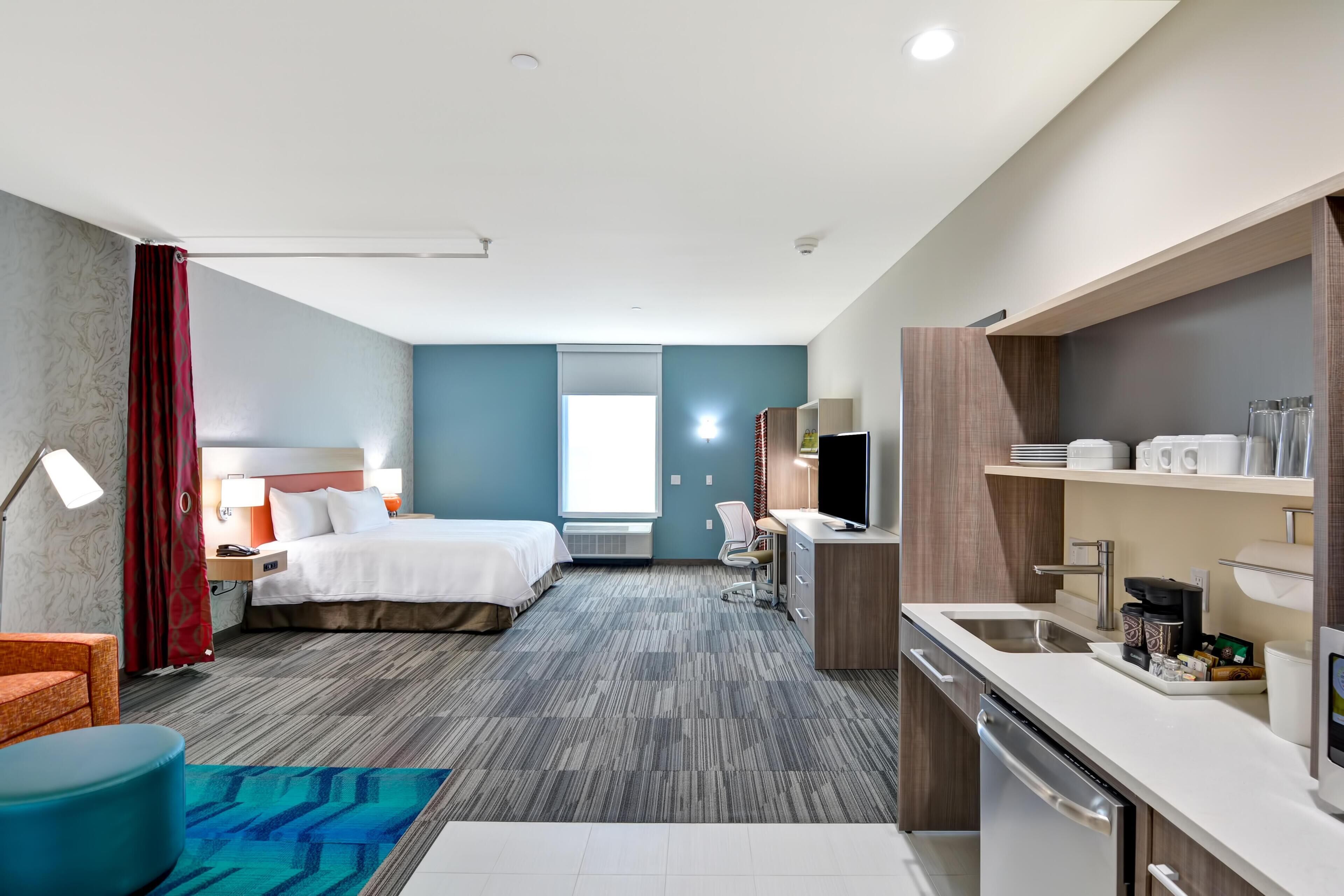 A hotel room with two beds, a desk, a kitchenette, and a bathroom.