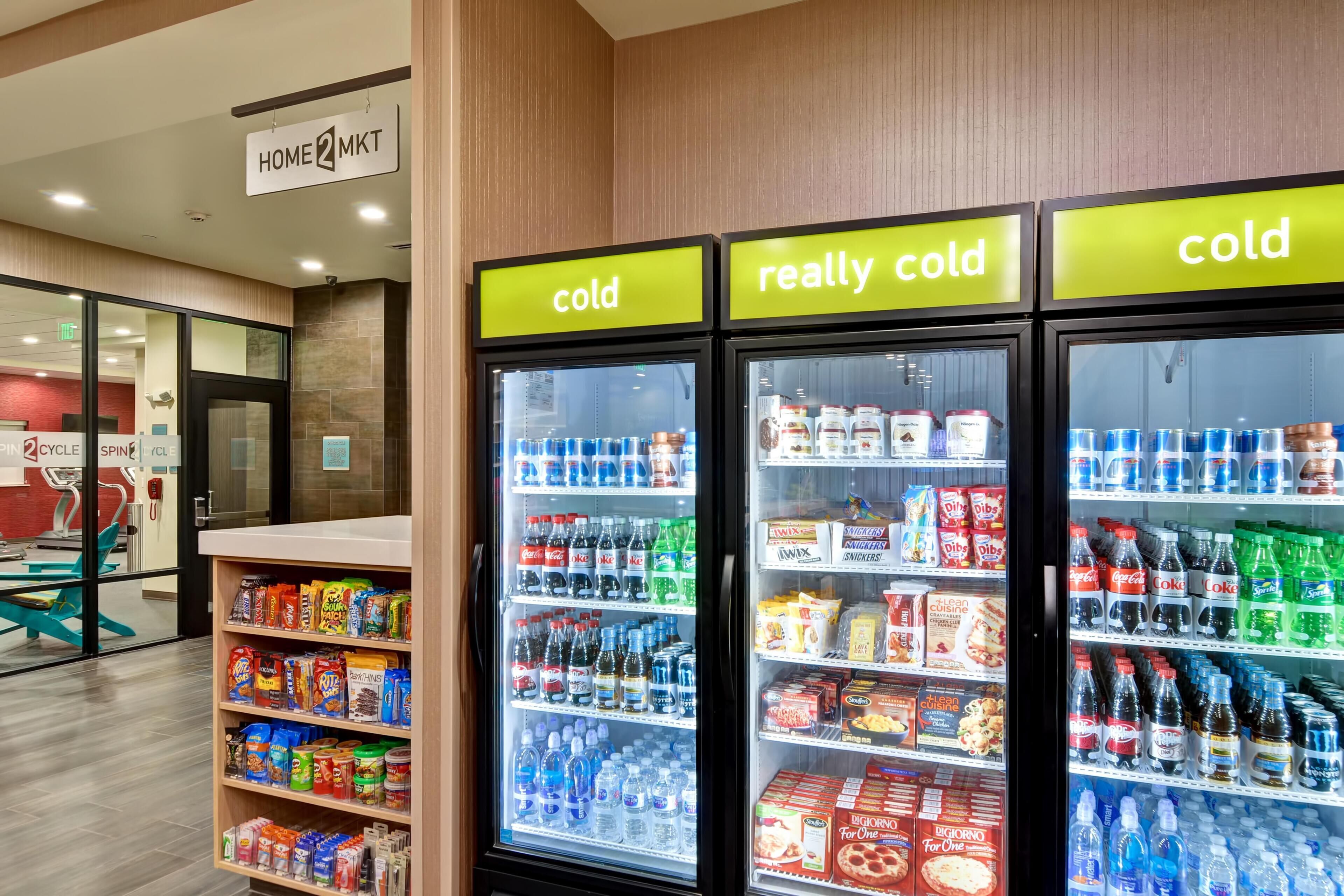 A hotel lobby with a reception desk, a sign for 'HOME 2 MKT', and three refrigerated display cases labeled 'cold', 'really cold', and 'cold'.
