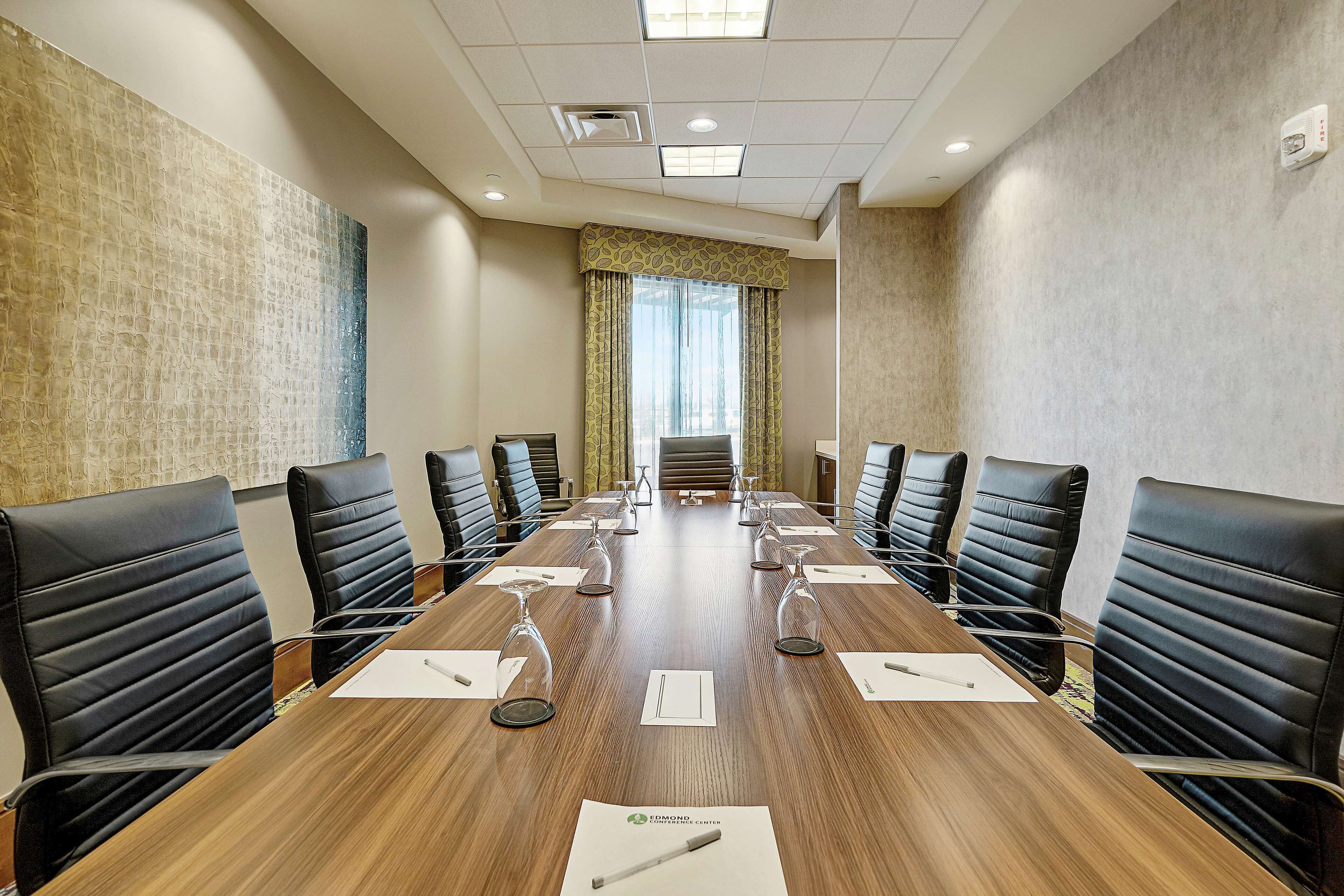 A conference room with a long table, black leather chairs, and a large window with curtains.