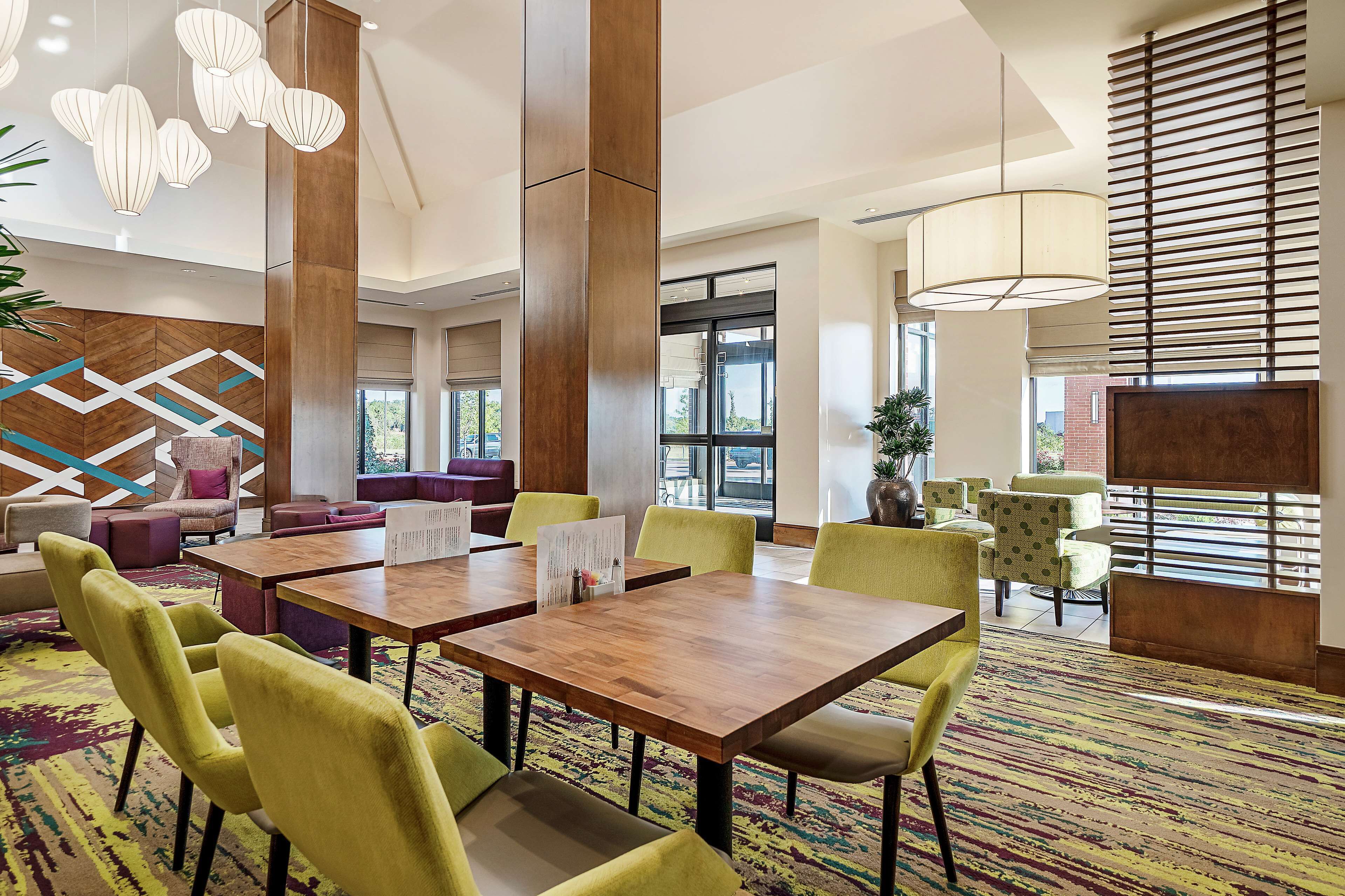Eine moderne Hotellobby mit großem Essbereich, bequemen Sitzgelegenheiten und großen Fenstern, die für natürliches Licht sorgen.