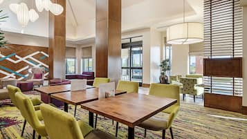 Eine moderne Hotellobby mit großem Essbereich, bequemen Sitzgelegenheiten und großen Fenstern, die für natürliches Licht sorgen.