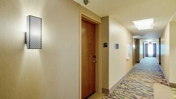 A hotel hallway with a patterned carpet, a wooden door, and a wall-mounted light fixture.