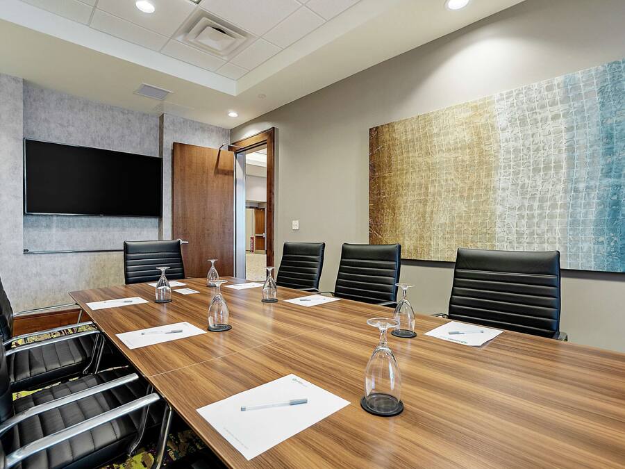 Une salle de conférence avec une longue table en bois, six chaises en cuir noir et un grand téléviseur à écran plat fixé au mur.