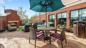An outdoor patio with a brick fireplace, wicker furniture, and a large umbrella. - Hilton Garden Inn Edmond / Oklahoma City North, OK (Edmond)