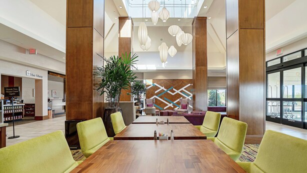 A spacious lobby with a long wooden conference table, green upholstered chairs, and a modern chandelier. - Hilton Garden Inn Edmond / Oklahoma City North, OK (Edmond)